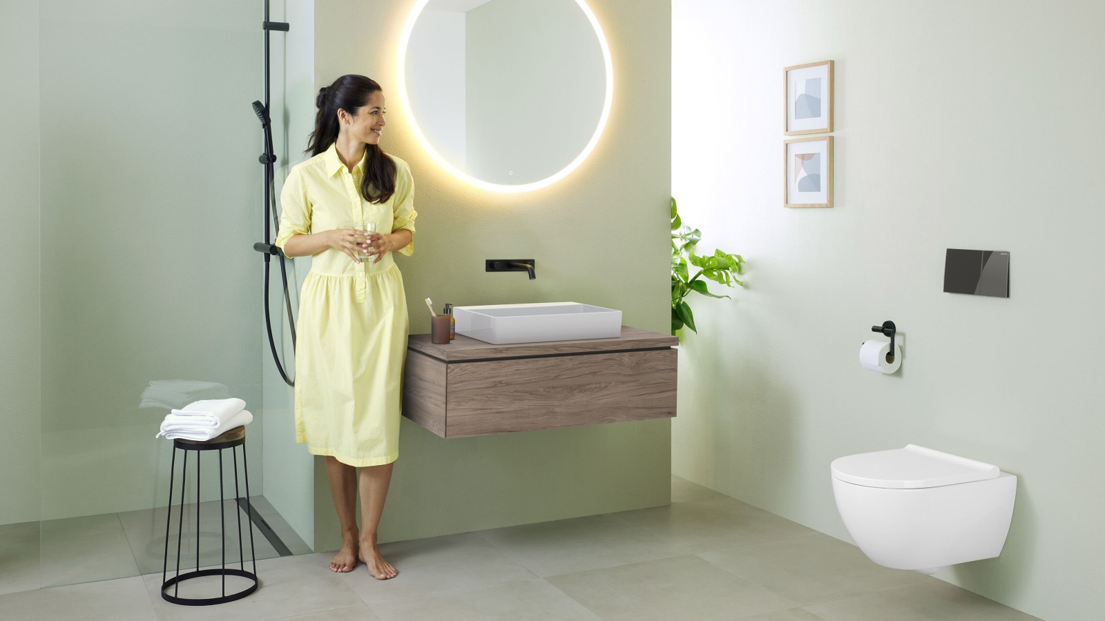Woman in yellow dress standing in front of mint green bathroom with furniture and bathroom ceramics from Geberit and black taps. Woman in yellow dress standing in front of mint green bathroom with furniture and bathroom ceramics from Geberit and black taps.