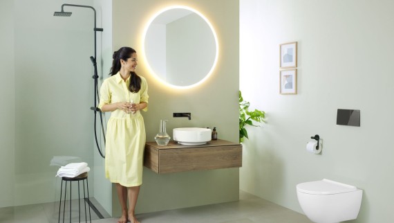 Woman in yellow dress standing in front of mint green bathroom with furniture and bathroom ceramics from Geberit and black taps.