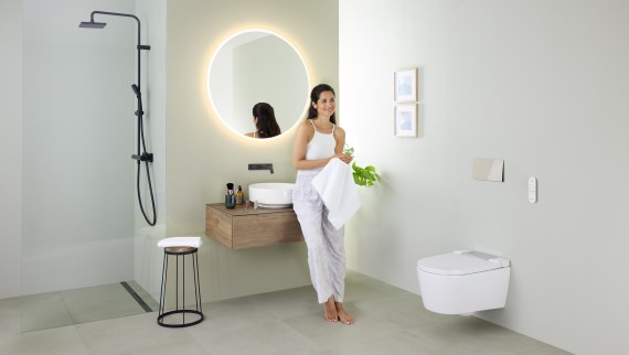 Woman leaning on a washbasin in a bathroom with Geberit AquaClean Sela shower toilet and Geberit VariForm washbasin and furniture