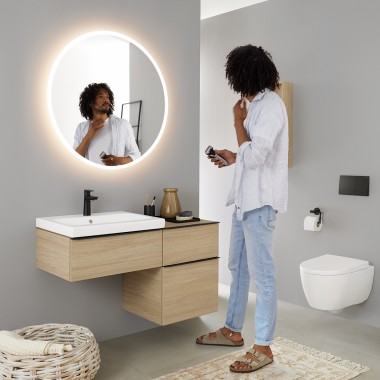 Man looking at himself in a round illuminated Geberit Option mirror