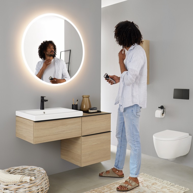 Man looking at himself in a round illuminated Geberit Option mirror